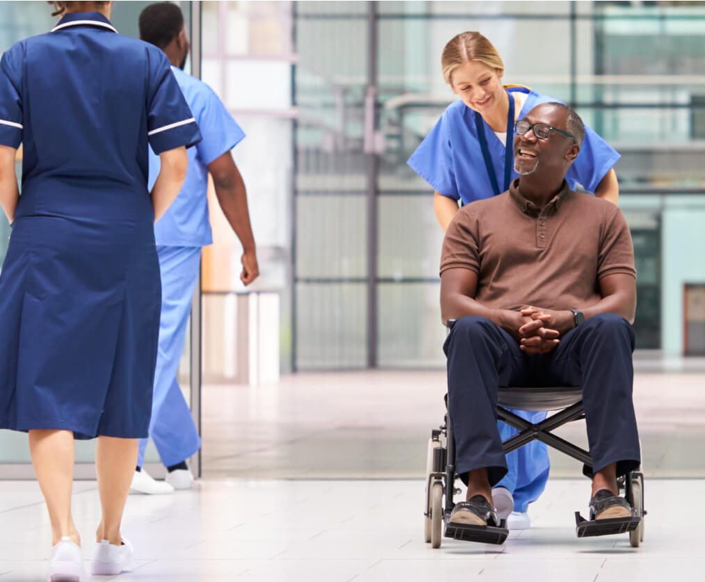 A man smiling while being pushed in a wheelchair by a female nurse